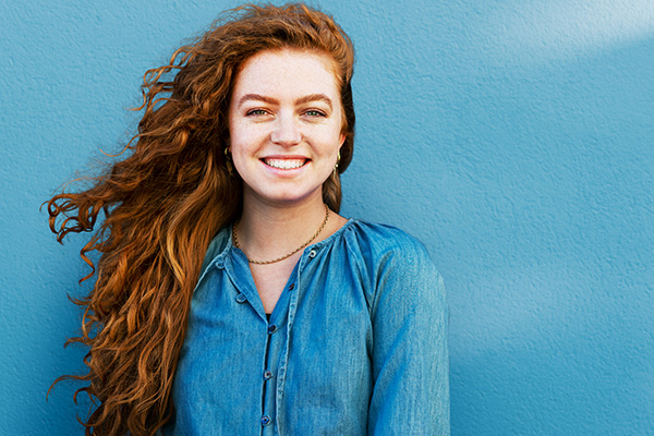 A curly redheaded girl standing against a textured blue wall