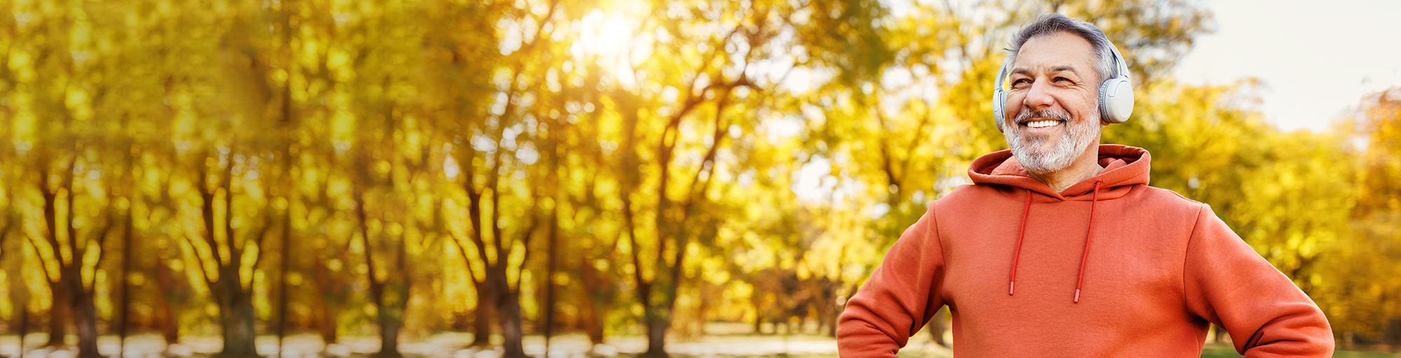 Grey haired middle-aged man wearing headphones jogging through a trail in the forest