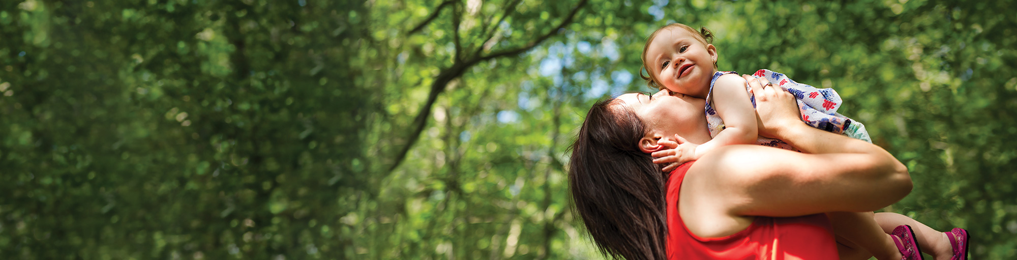 Mother and kissing and hugging toddler age daughter in a green lush forest